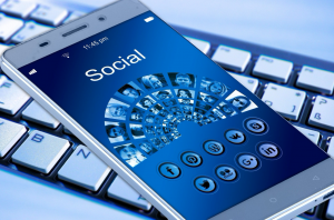 Smartphone with “Social” on the screen & various social media icons, sitting on computer keyboard; image by Geralt, via Unsplash.com.