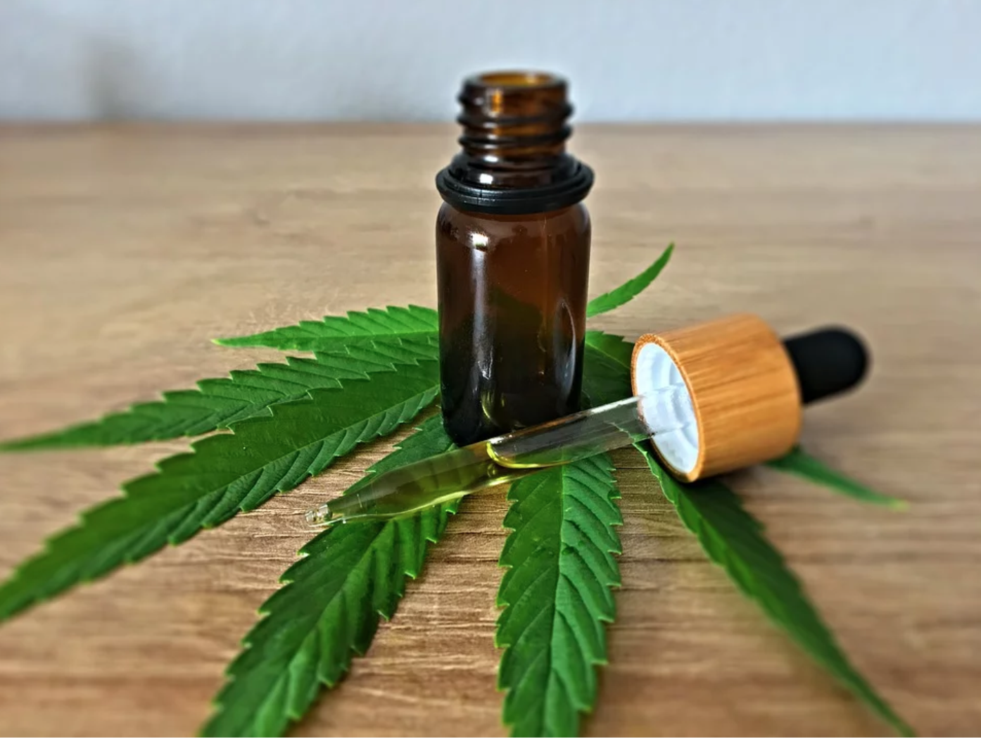 Marijuana leaf on wooden surface, with a brown bottle and eyedropper on the leaf; image by CBD-Infos-Com, via Pixabay.com.