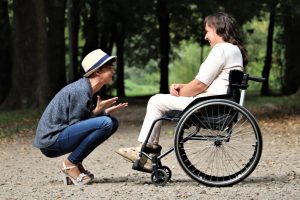 Woman seated in wheelchair facing woman in hat; image by Judita Tamošiūnaitė, via Pexels.com.