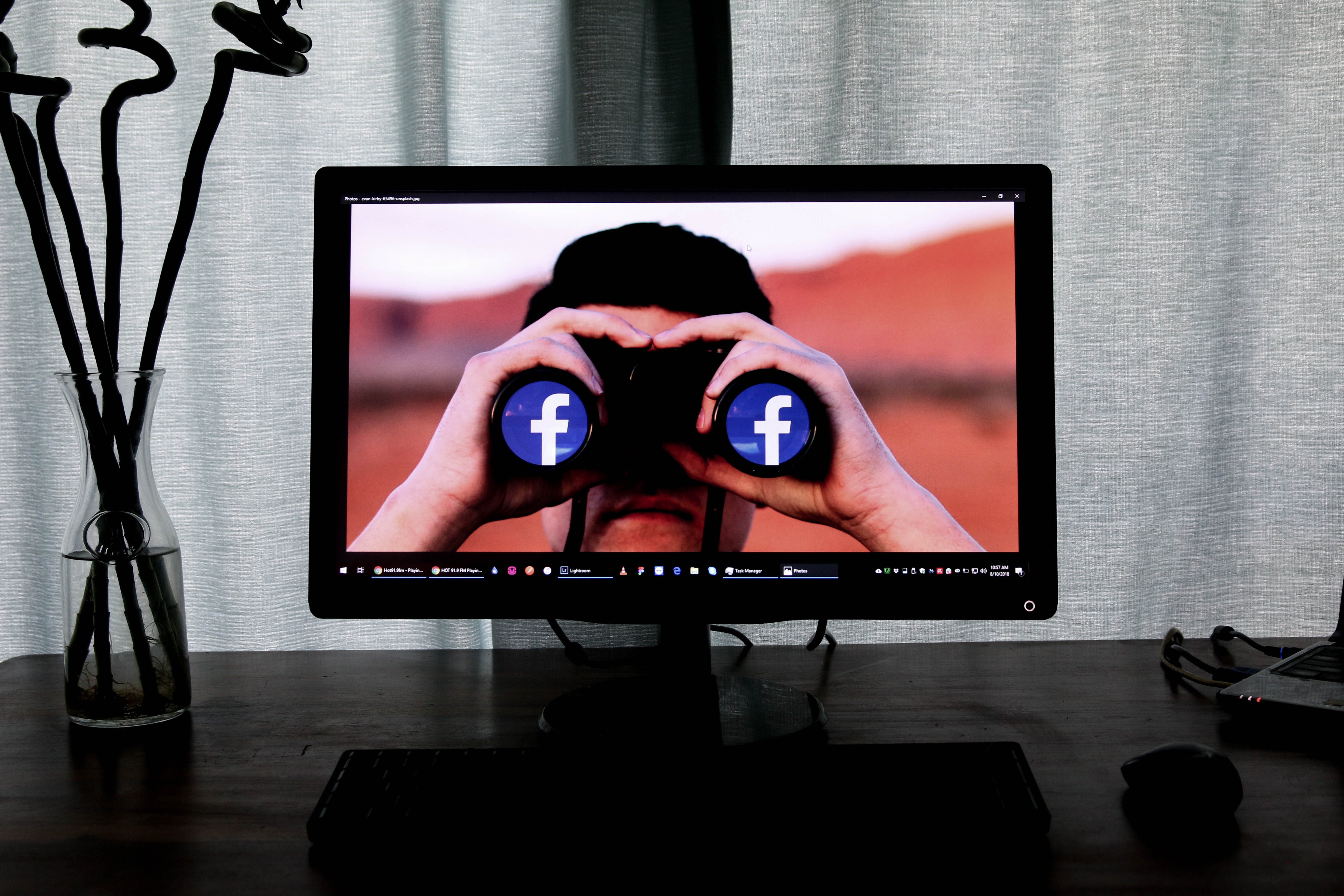 Computer monitor showing man with binoculars staring out at viewer. Lenses of binoculars are the Facebook logo. Image by Glen Carrie, via Unsplash.com.