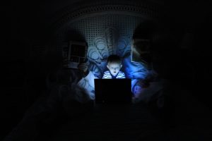 Family in bed, parents reading and child on laptop; image by Ludovic Toinel, via Unsplash.com.