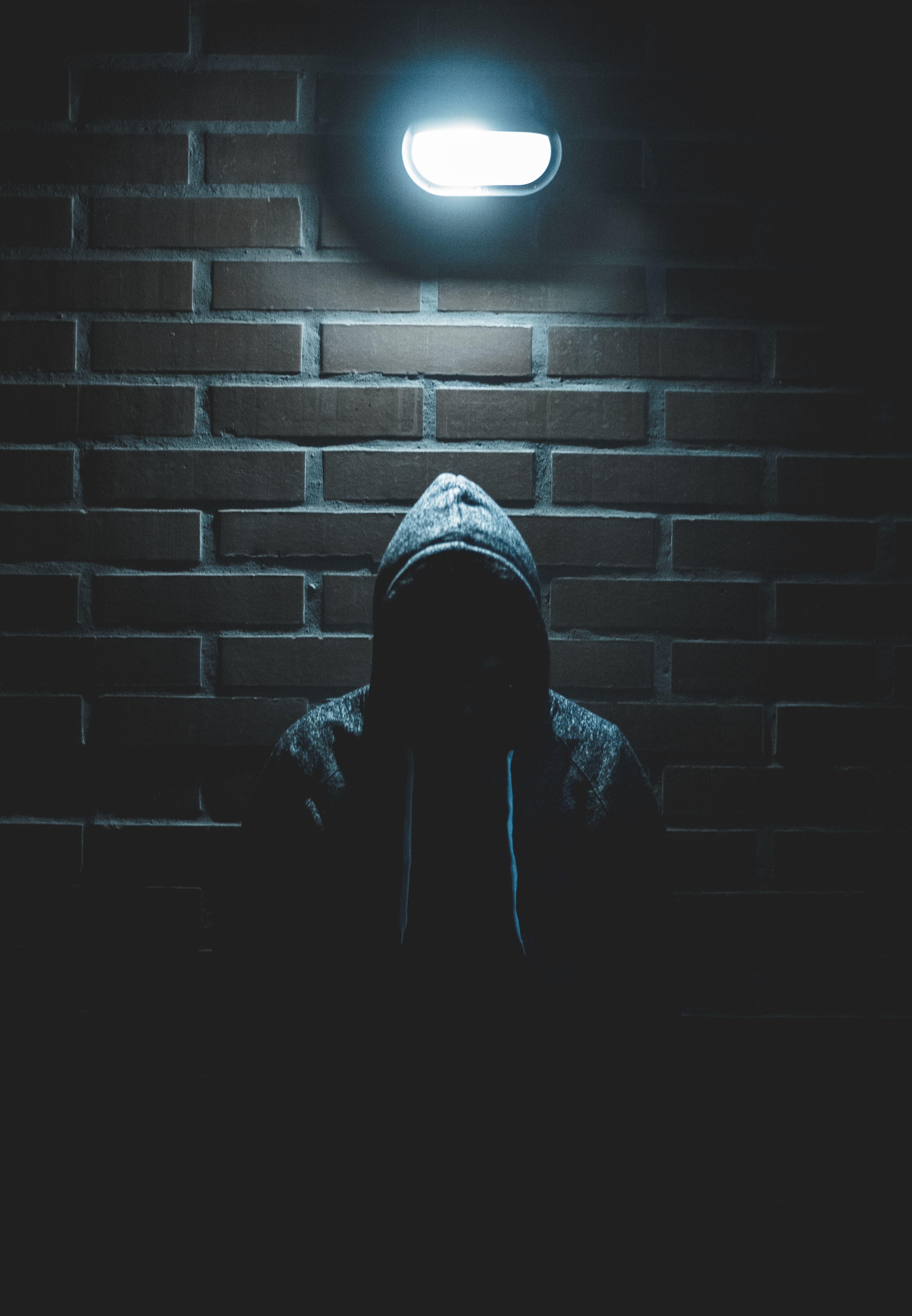 Man in hoodie standing in dark alley; image by Luis Villasmil, via Unsplash.com.
