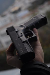 Man with black semi-automatic pistol in palm of hand; image by Roman Poberezhnik, via Unsplash.com.