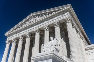 A classically designed stone building with Corinthian columns and a carved frieze, with a clear blue sky in the background.