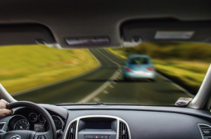 Man driving, in-focus view of dash with out-of-focus view of car ahead; image by JoeNomi 1961, via Wikimedia Commons, CC0.