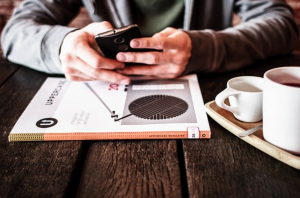 Man with smartphone and magazine at coffee shop; image by Free-Photos, via Pixabay.com.