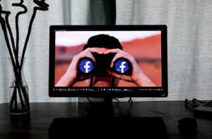 TV showing man using binoculars with lenses replaced by the Facebook logo; image by Glen Carrie, via Unsplash.com.
