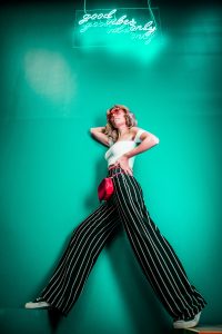 Woman in striped pants against green background with “Good Vibes Only” neon sign; image by Ahmed Carter, via Unsplash.com.