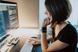 Woman sitting at a desk in front of coding computer screen; image by Kelly Sikkema, via Unsplash.com.