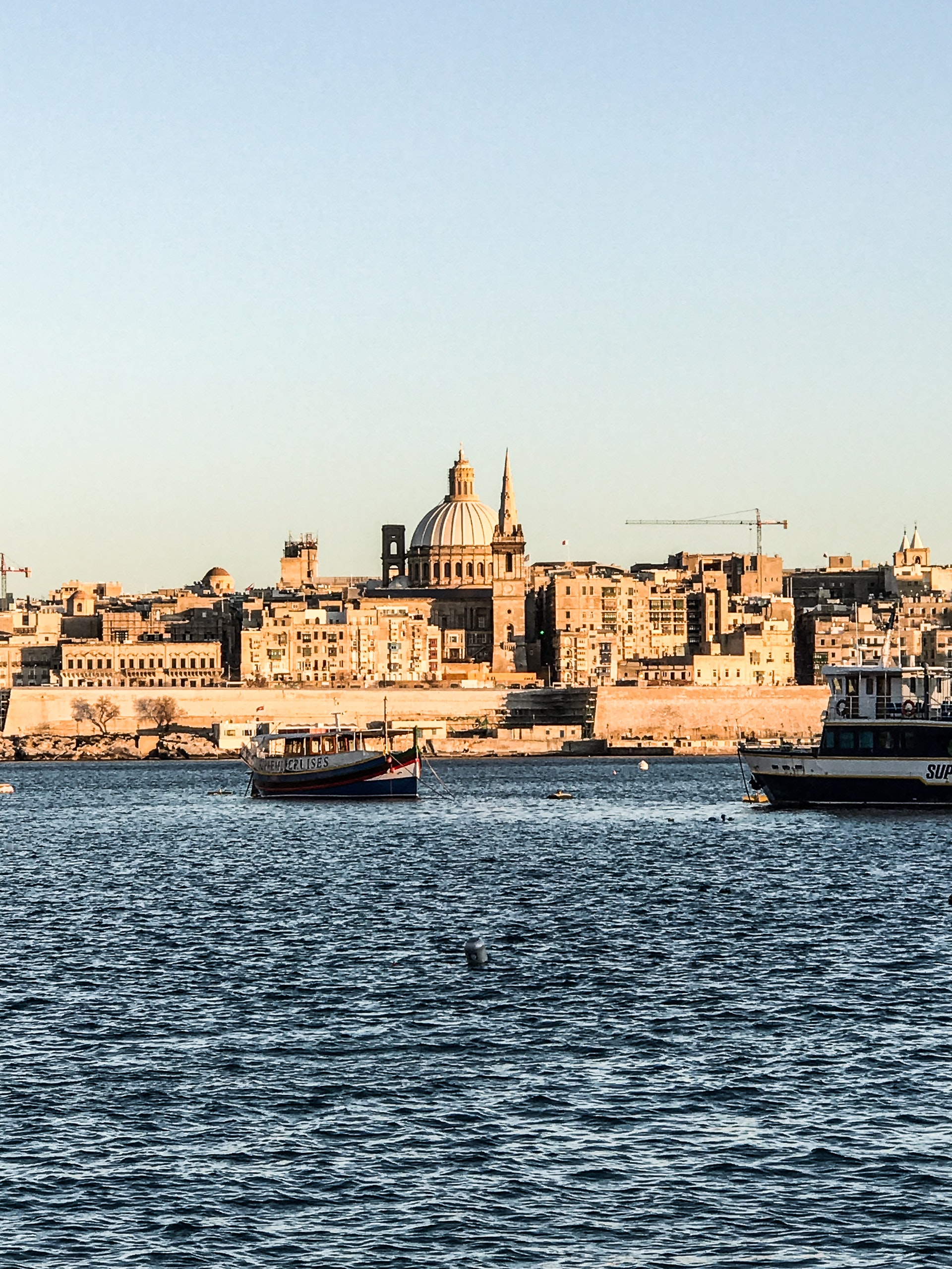 Two ships on the water in front of the beautiful architecture of Valletta, Malta; image by Ines Bahr, via Pexels.com.