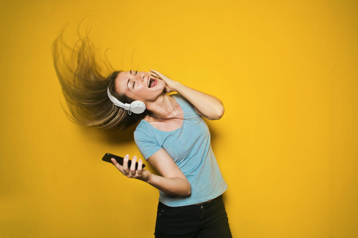Woman listening to music against a yellow background; image by Andrea Piacquadio, via Pexels.com.