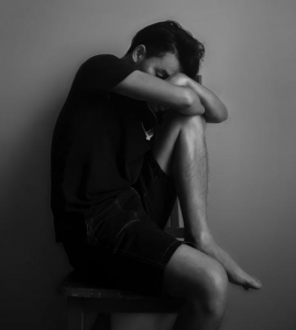 Grayscale image of man sitting next to a wall; image by Pixabay, via Pexels.com.