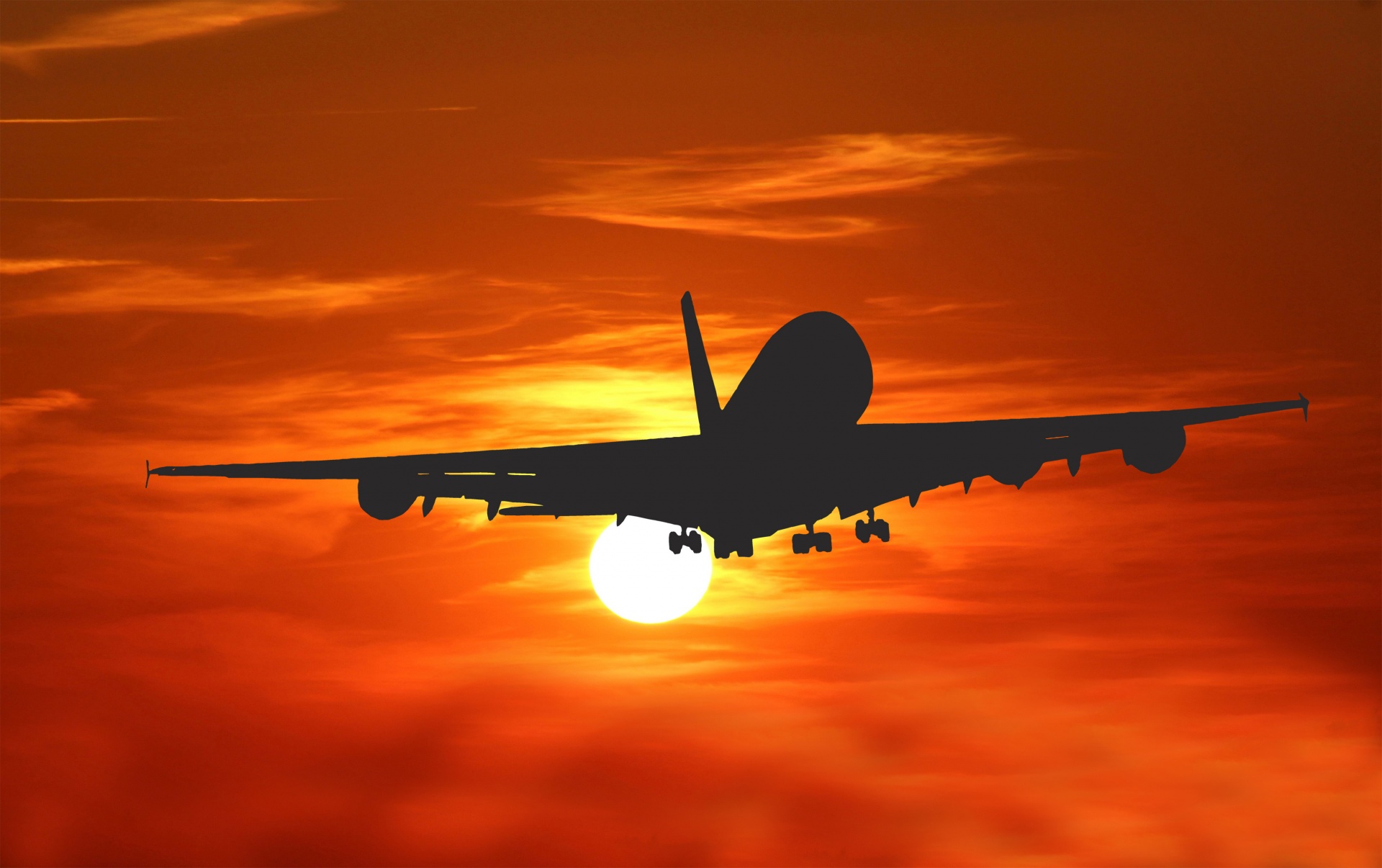 The silhouette of a commercial aircraft backed by a vivid sunset.