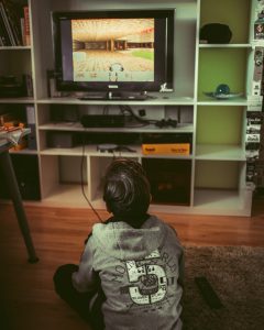 Boy sitting on floor near TV, playing video game; image by Albert Renn, via Unsplash.com.