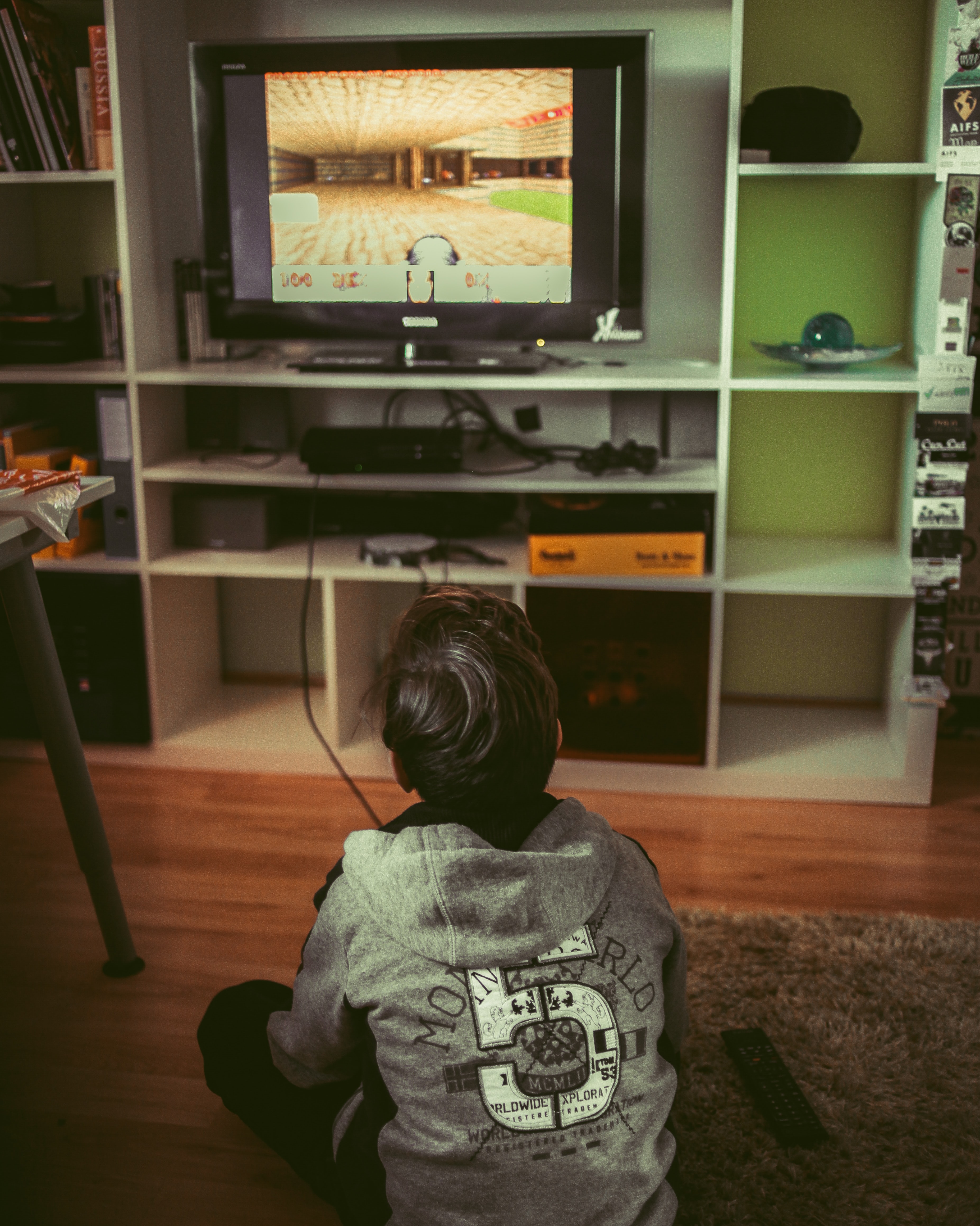 Boy sitting on floor near TV, playing video game; image by Albert Renn, via Unsplash.com.