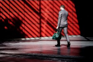 Man in suit carrying green bag and walking in front of red wall; image by Clem Onojeghuo, via Unsplash.com.