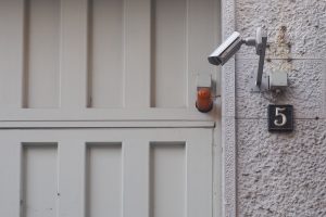 White wooden door near gray security camera; image by Josh Shaw, via Unsplash.com.