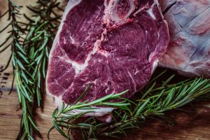 A raw cut of red meat surrounded by green herbs.