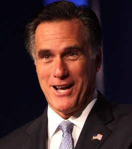 Mitt Romney grinning, wearing a dark suit.