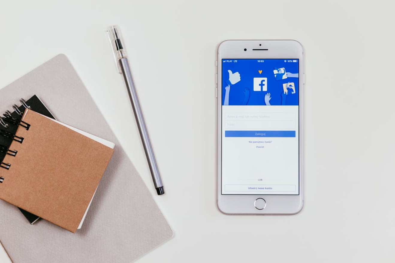 Notepads, pen, and smartphone with Facebook on the screen; image by freestocks.org, via Pexels.com.