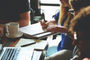 Students working at a table with coffee, notebooks, and laptops; image by Startupstockphotos, via Freepik.com.