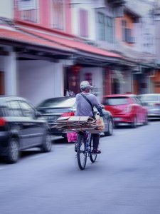 Man on bicycle riding past parked cars; image by Adeline Lee, via Unsplash.com.