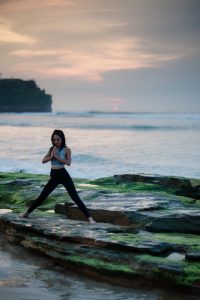 Woman doing yoga by the shore; image by bady qb, via Unsplash.com.