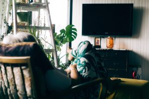 Woman sitting in chair in front of TV; image by John Tuesday, via Unsplash.com.