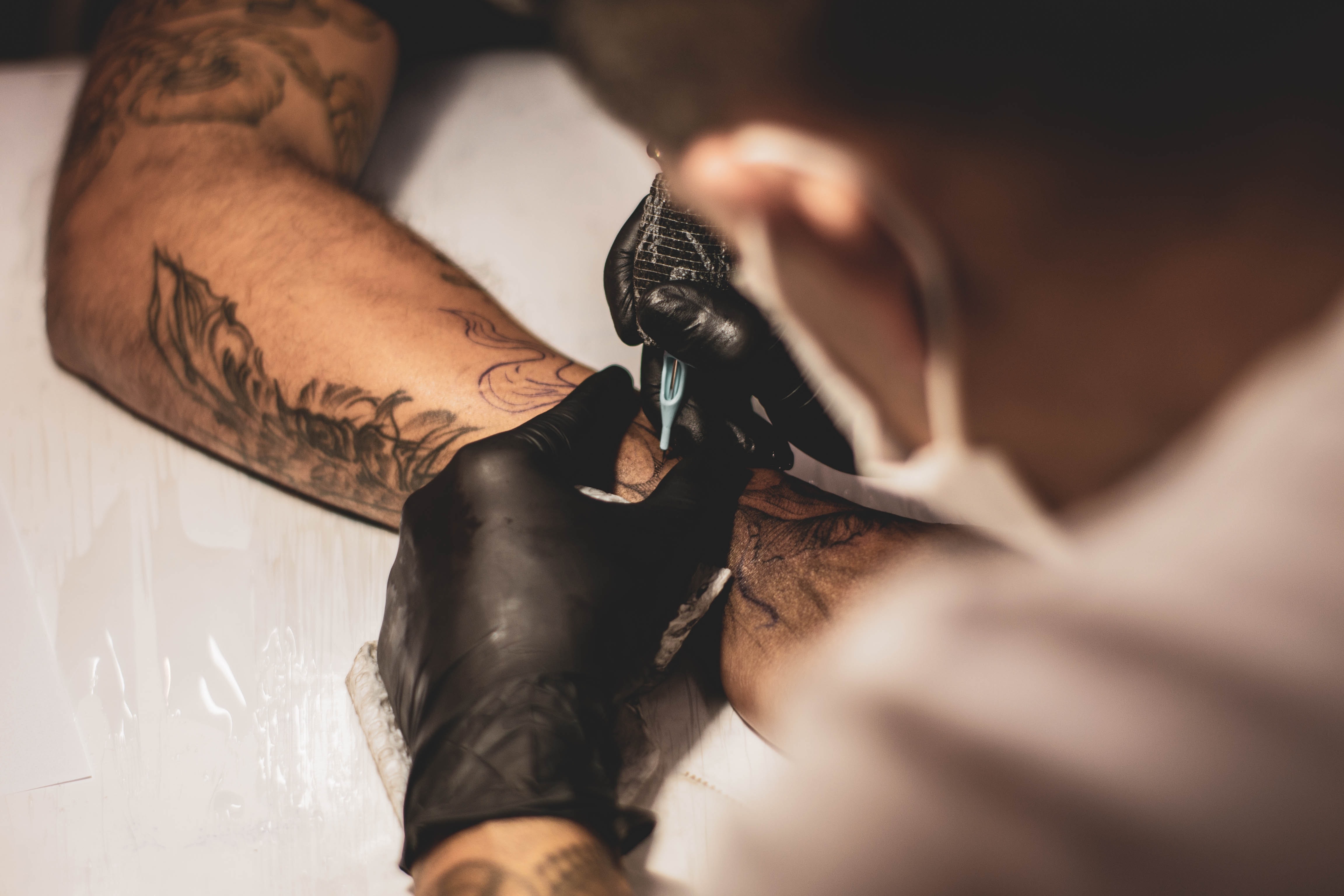 Tattoo artist working on client; image by Lucas Lenzi, via Unsplash.com.