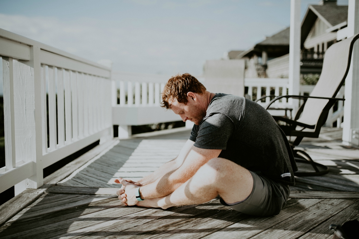 Man doing seated stretches on a deck; image by Scott Broome, via Unsplash.com.