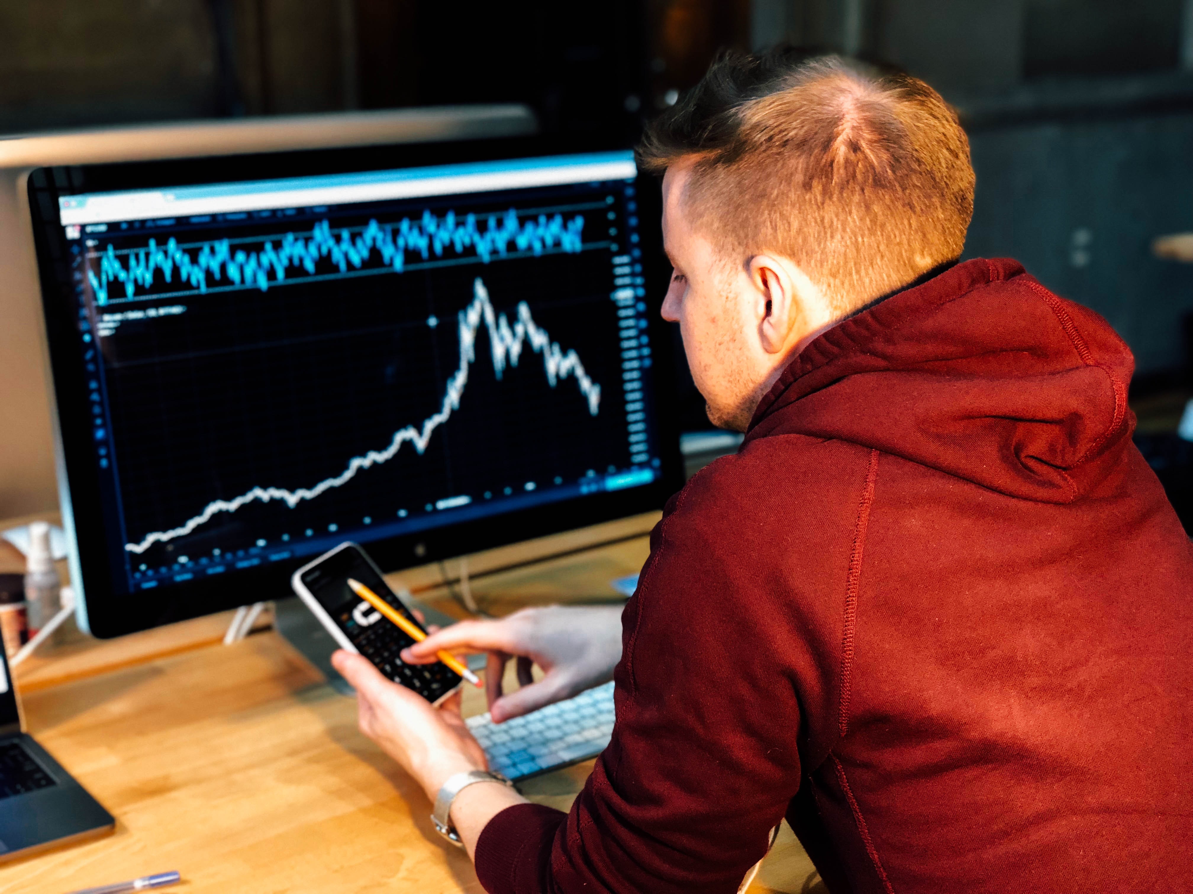 Man with laptop and phone working on investing; image by Chris Liverani, via Unsplash.com.