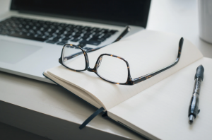 Laptop, notebook, pen, and reading glasses; image by Trent Erwin, via Unsplash.com.