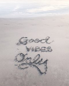 “Good Vibes Only” written in the sand by the sea; image by Ashley Whitlatch, via Unsplash.com.