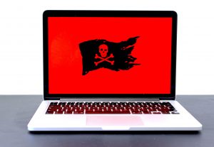 Laptop displaying a pirate flag / jolly roger on a red screen, possibly indicating malware, hackers or a different computer problem. Image by Michael Geiger, via Unsplash.com.