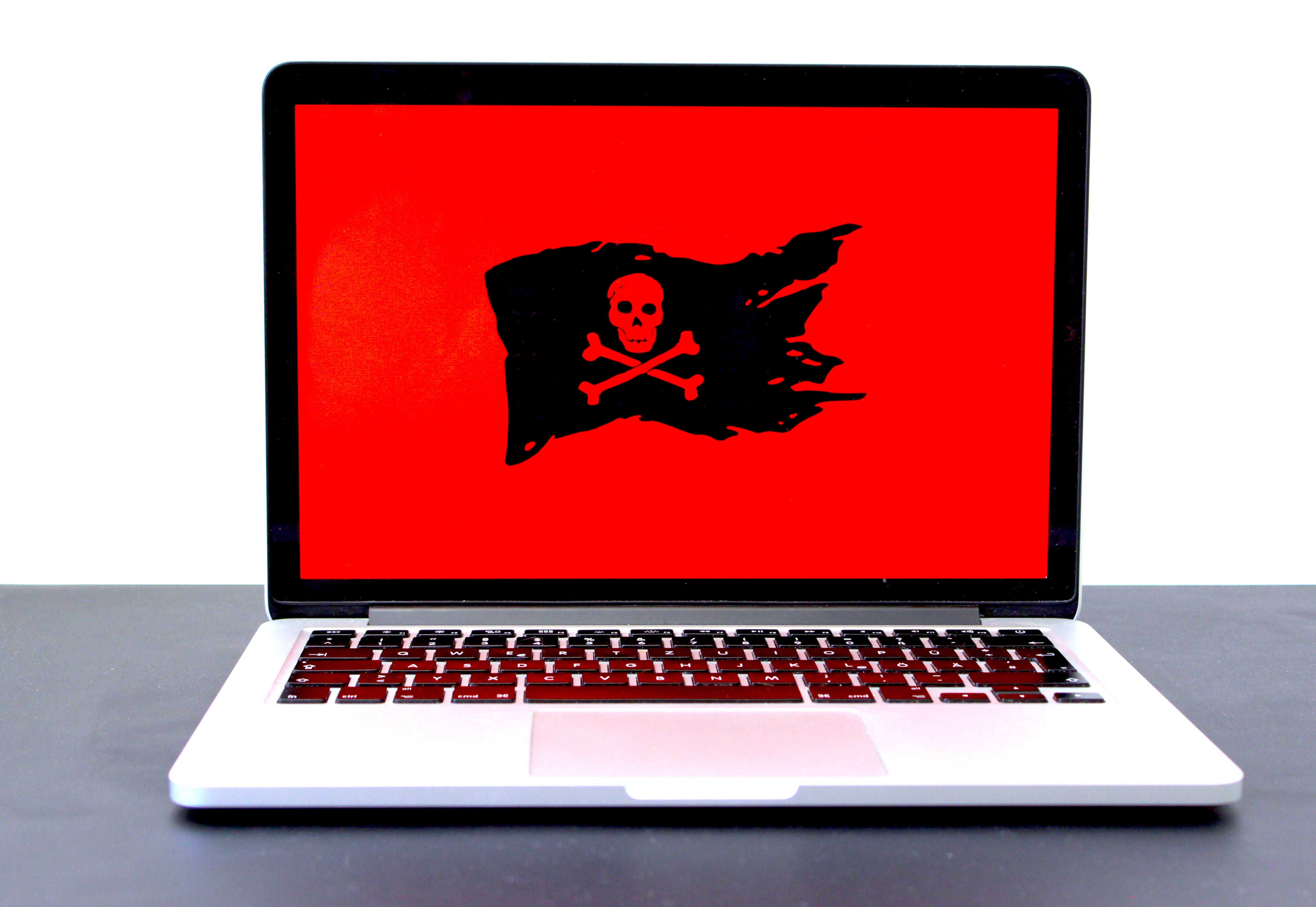 Laptop displaying a pirate flag / jolly roger on a red screen, possibly indicating malware, hackers or a different computer problem. Image by Michael Geiger, via Unsplash.com.