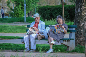 Older couple reading tabloids on park bench; image by besnopile, via Pixabay.com.