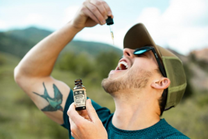 Colorado man taking hemp extract oil from a tincture outside; image by R+R Medicinals, via Unsplash.com.