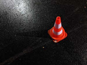 Traffic cone on dark, wet pavement; image by Lucian Alexe, via Unsplash.com.