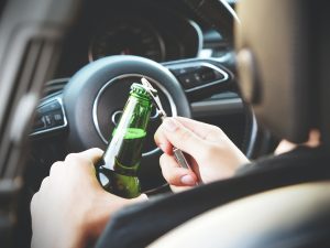 Plain view: Man opening bottle behind the wheel; image by energe.com, via Pexels.com.