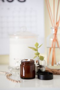 Brown jar of cream, green plant on white surface; image by Maddi Bazzocco, via Unsplash.com.