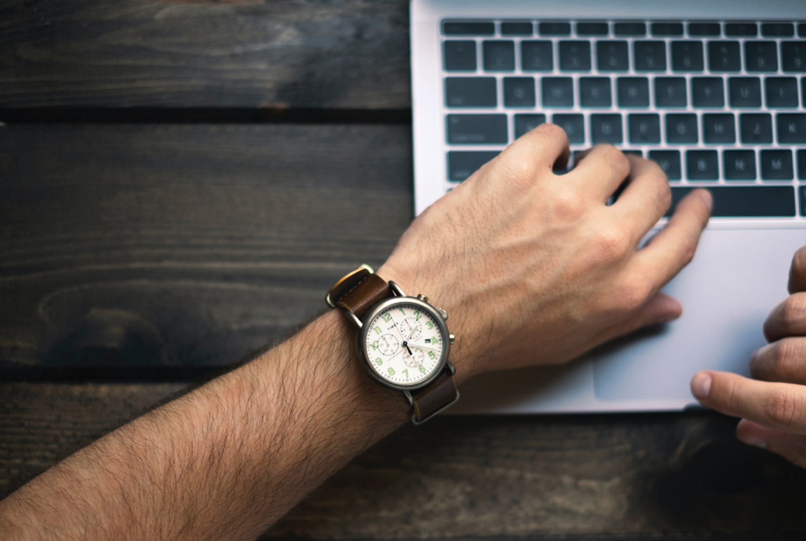 Man wearing a watch using a laptop; image by Brad Neathery, Via Unsplash.com.