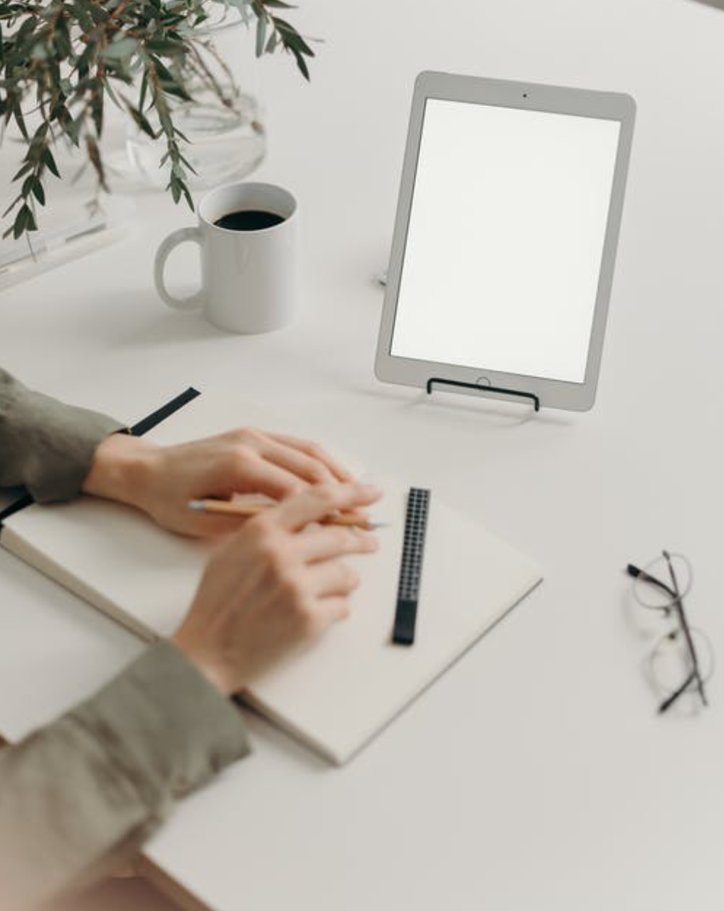 Woman at desk with paper, tablet, and glasses; image by CottonBro, via Pexels.com.