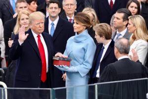 Donald Trump takes the oath of office, hand on two Bibles, with wife Melania, son Barron, and a crowd of others around him.