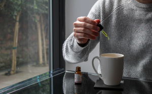 Man putting CBD oil in tea; image by Evopure CBD, via Unsplash.com.