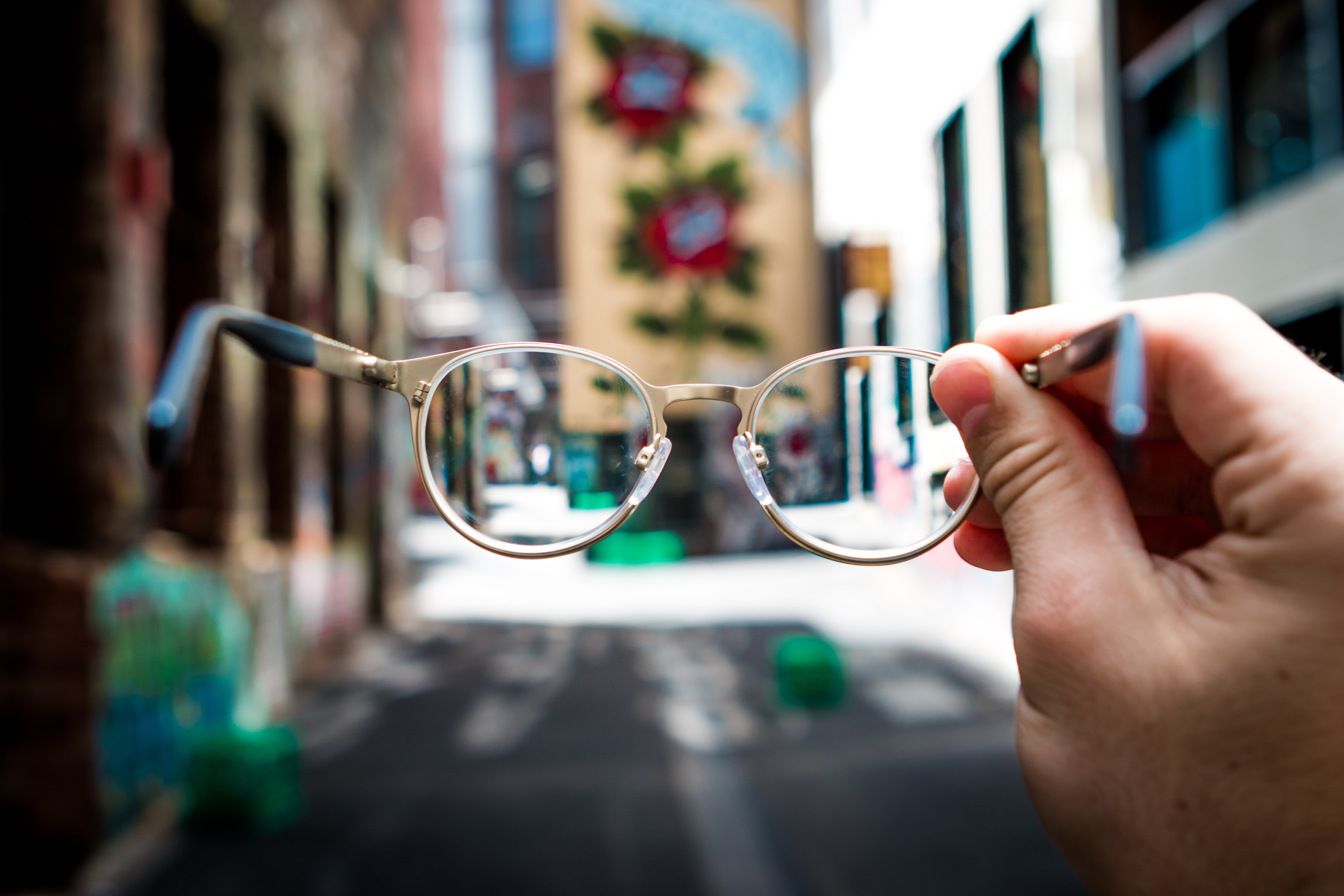 Man holding pair of glasses, surrounding scenery blurry; image by Josh Cala...