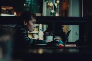 Woman in a cafe, looking at a laptop screen; image by Alex Kalligas, via Unsplash.com.