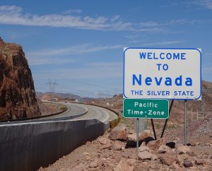 A road sign that says "Welcome to Nevada" by an empty freeway and rocky landscape.