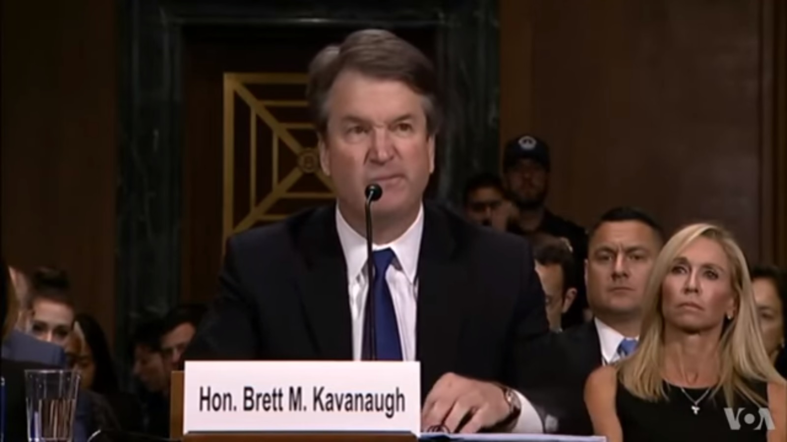 A middle-aged man in a suit sits at a desk during Senate hearings.