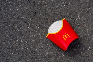 An empty McDonald's French fry sleeve resting on a tarmac surface.