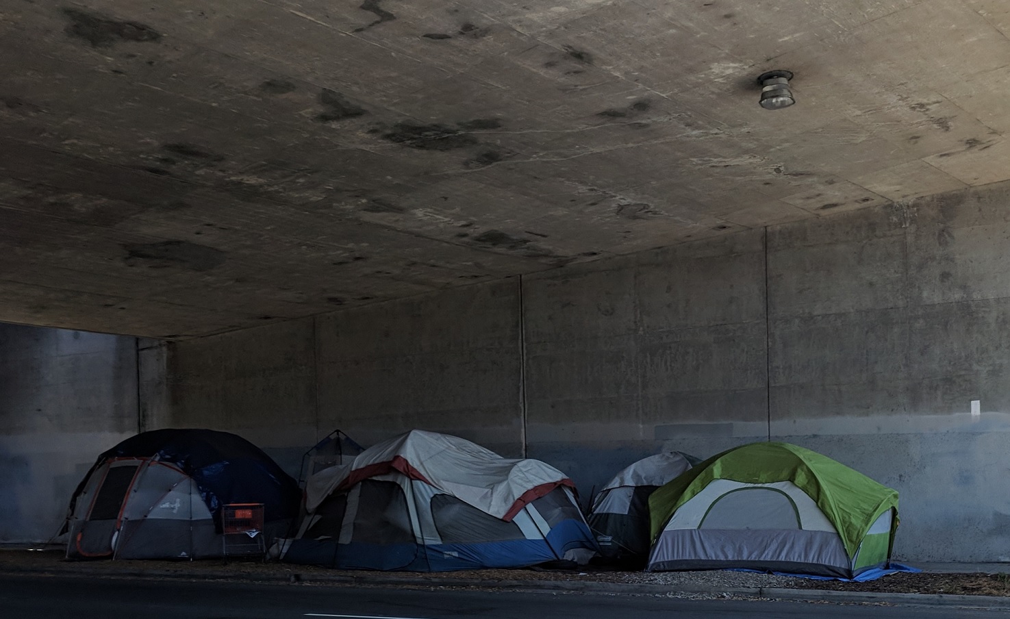 Several tents packed closely together under an overhanging concrete structure.